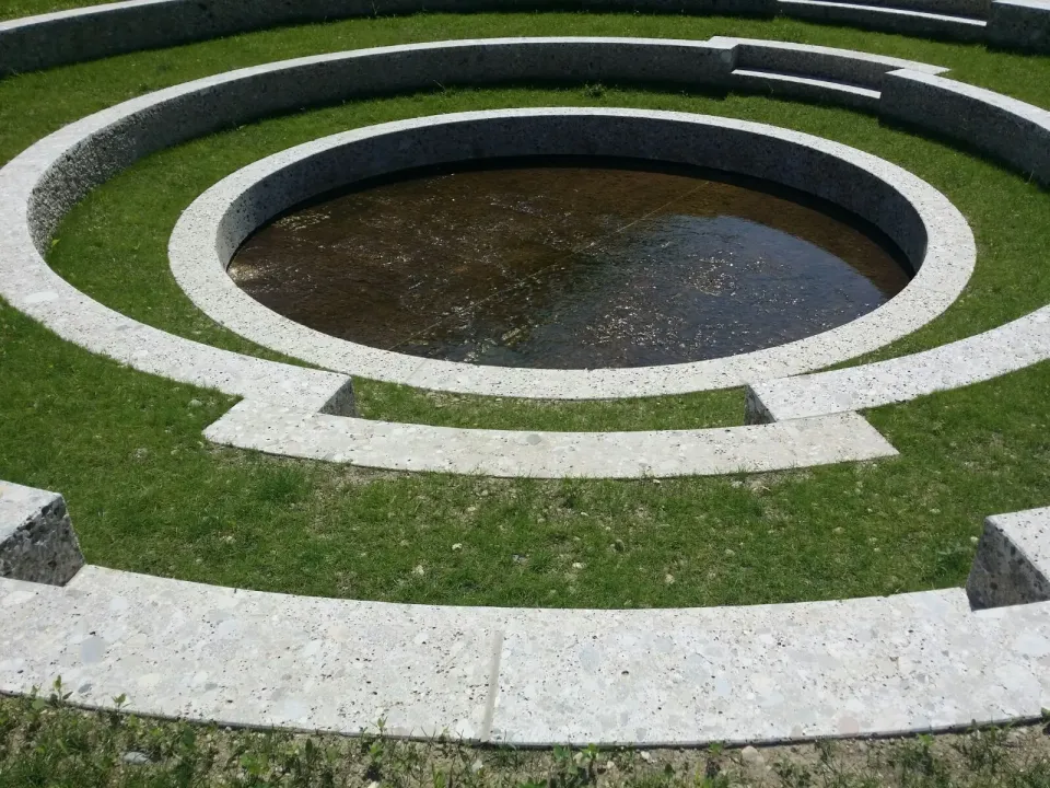 Runde Brunnenanlage aus Naturstein mit sauber verfugten Ringen im Rasen